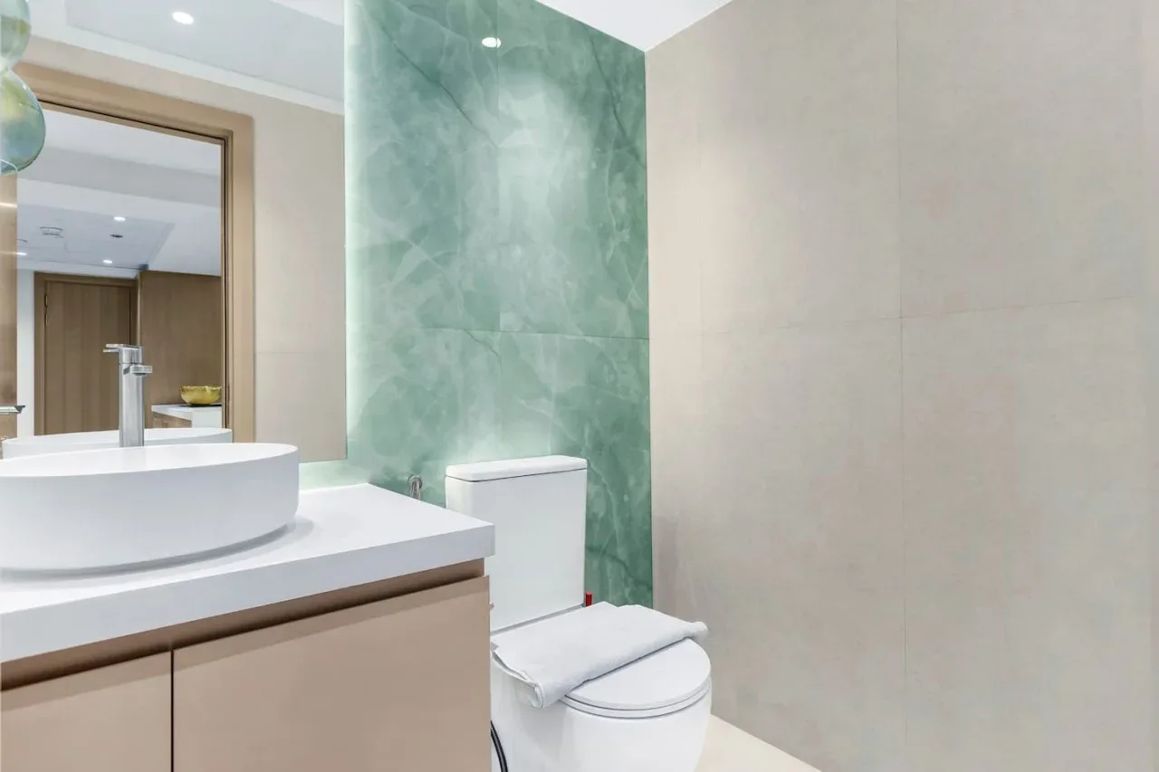 A bathroom with a vessel sink, toilet, and green accent wall.