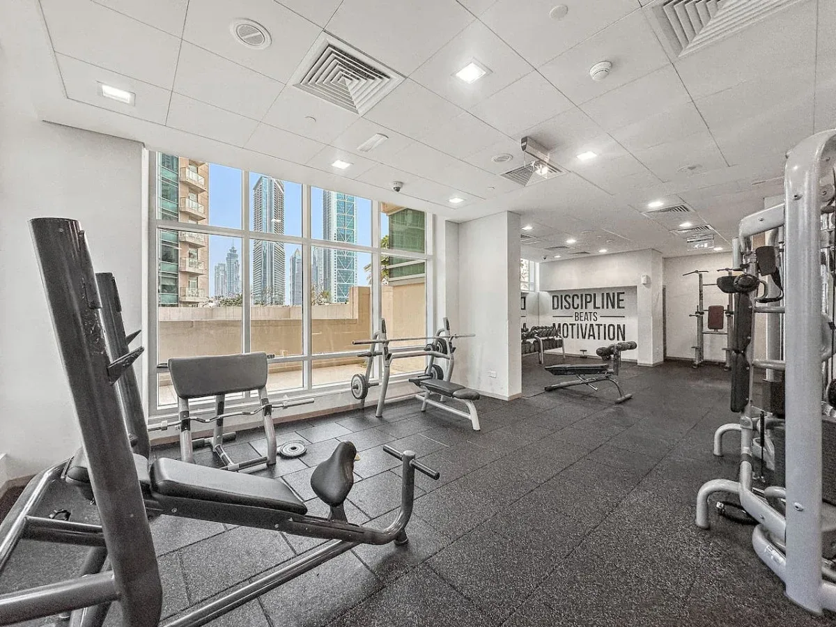 A gym with exercise machines, weight benches, and large windows.