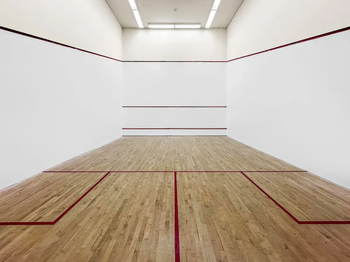 An indoor squash court with a wooden floor and red boundary lines.