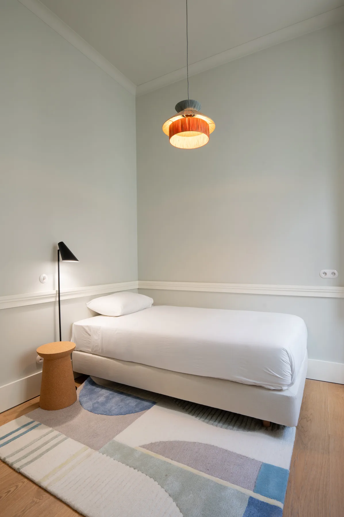 Un dormitorio con una cama individual, una lámpara de mesilla y una alfombra estampada.