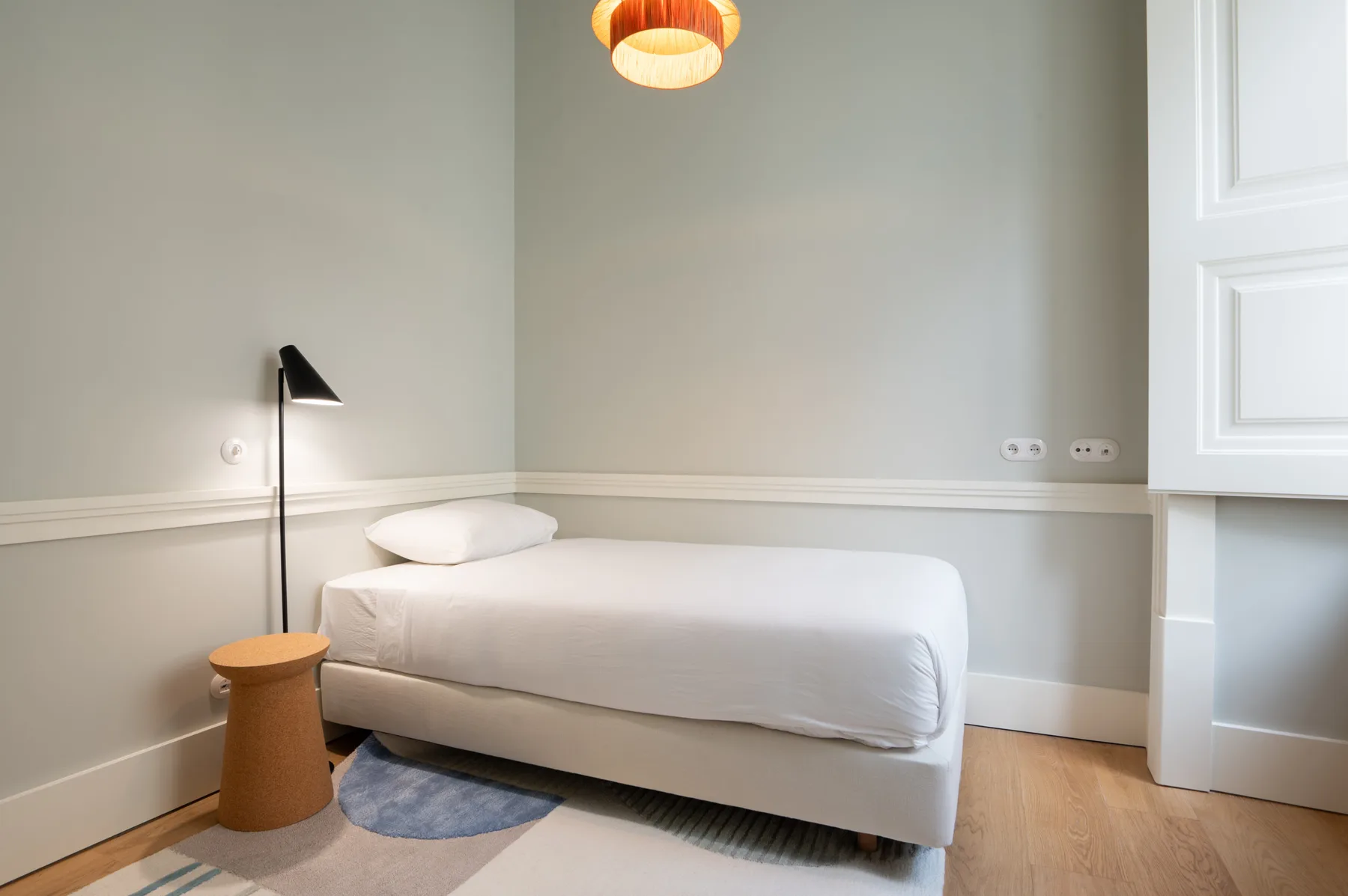 Un dormitorio con una cama blanca, una mesita de noche y una lámpara de pie.