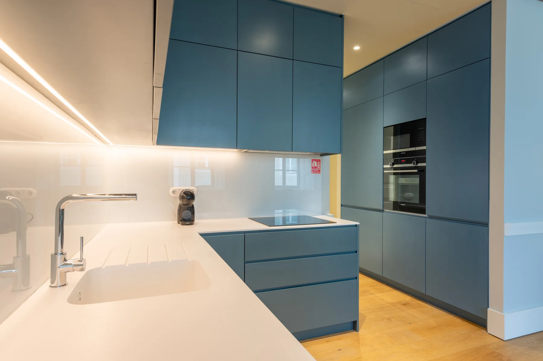 Una cocina moderna con armarios azules, una encimera blanca y electrodomésticos integrados.