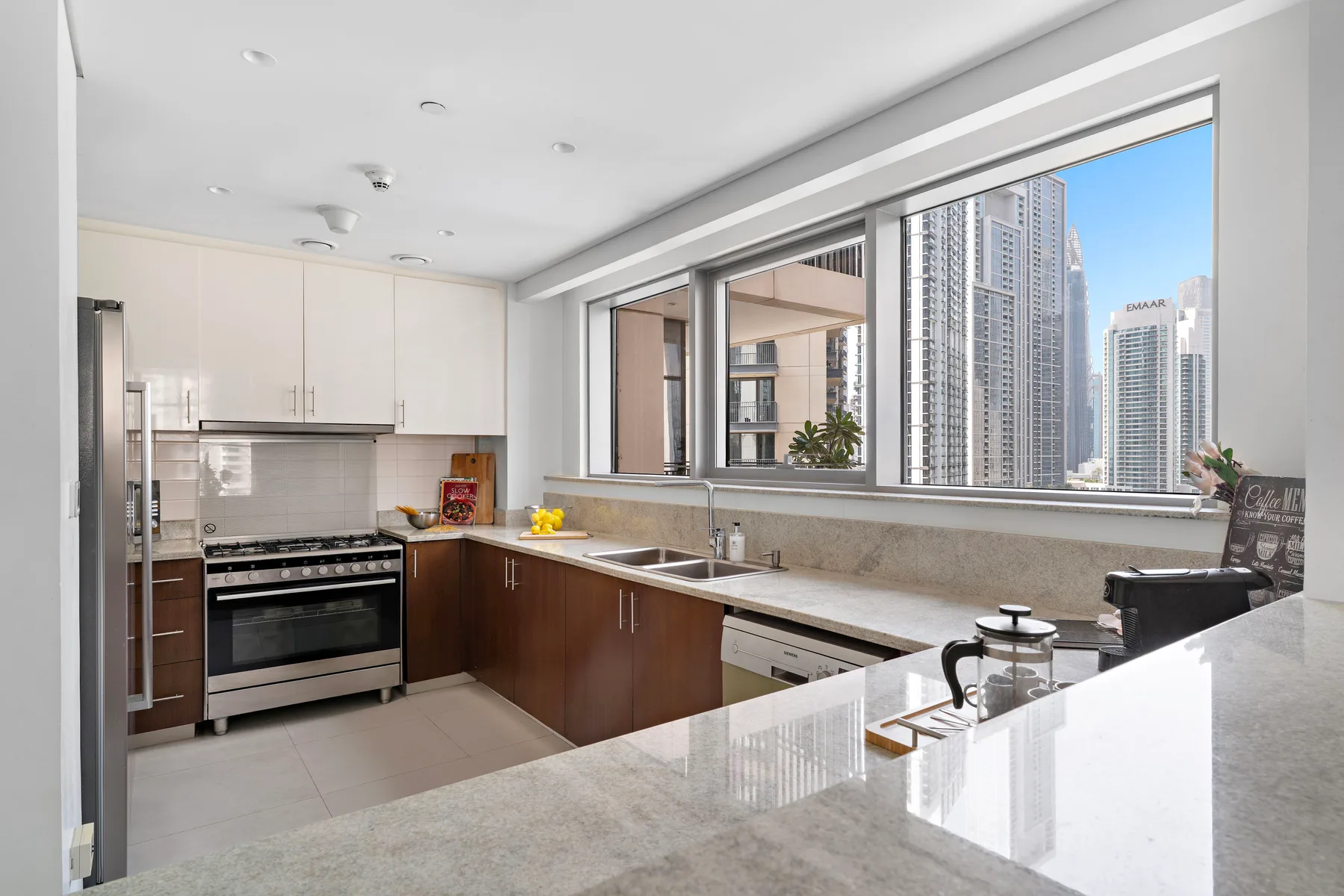 Una cocina moderna con gabinetes oscuros y grandes ventanales con vistas a edificios altos.