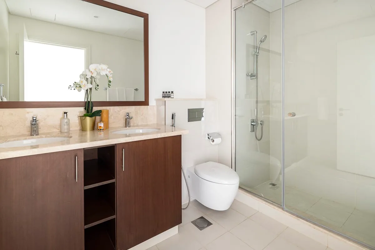 Un baño luminoso con lavabo, espejo, inodoro y ducha de cristal.
