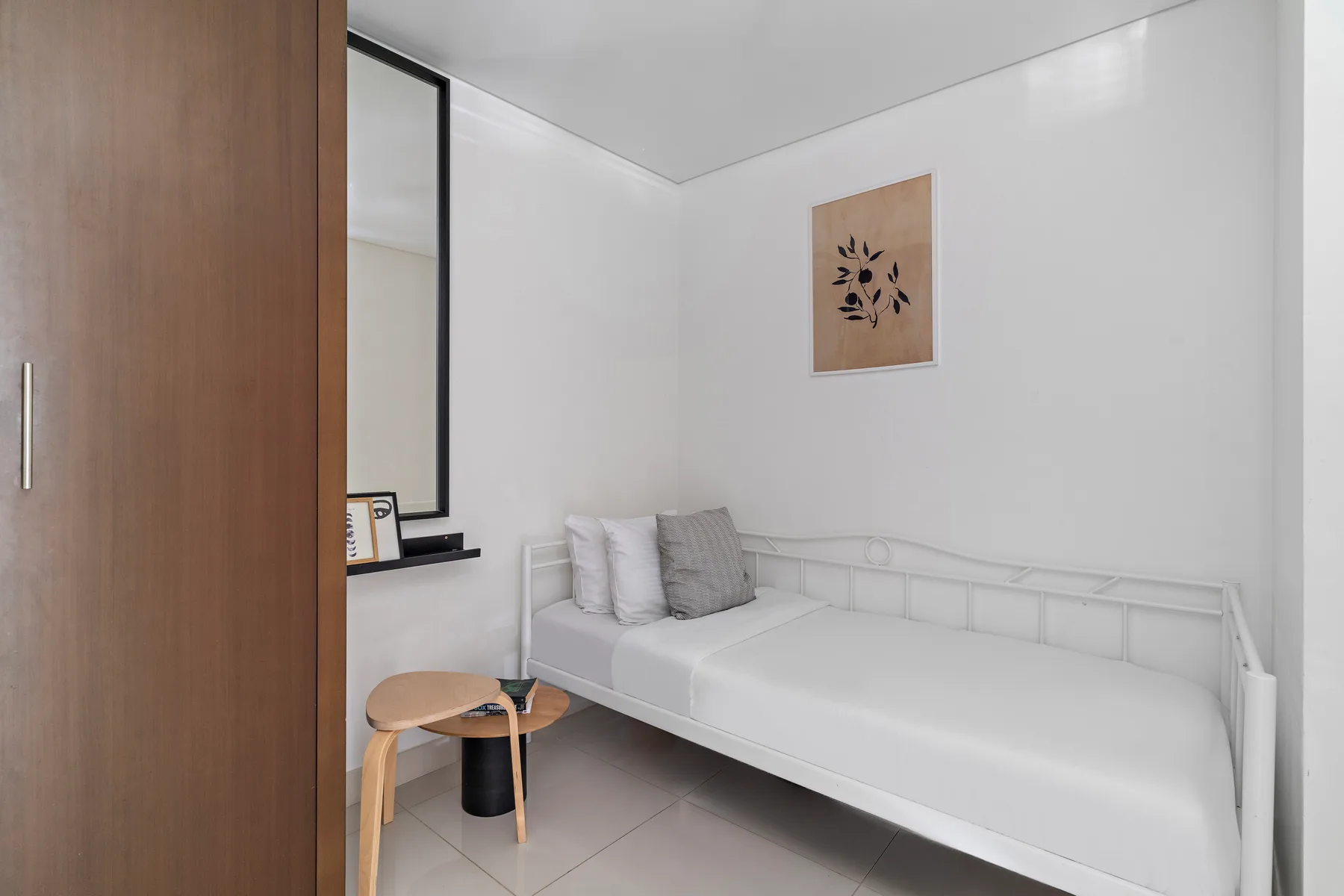 Un dormitorio luminoso con una cama blanca, una ventana y una pequeña mesa de madera.
