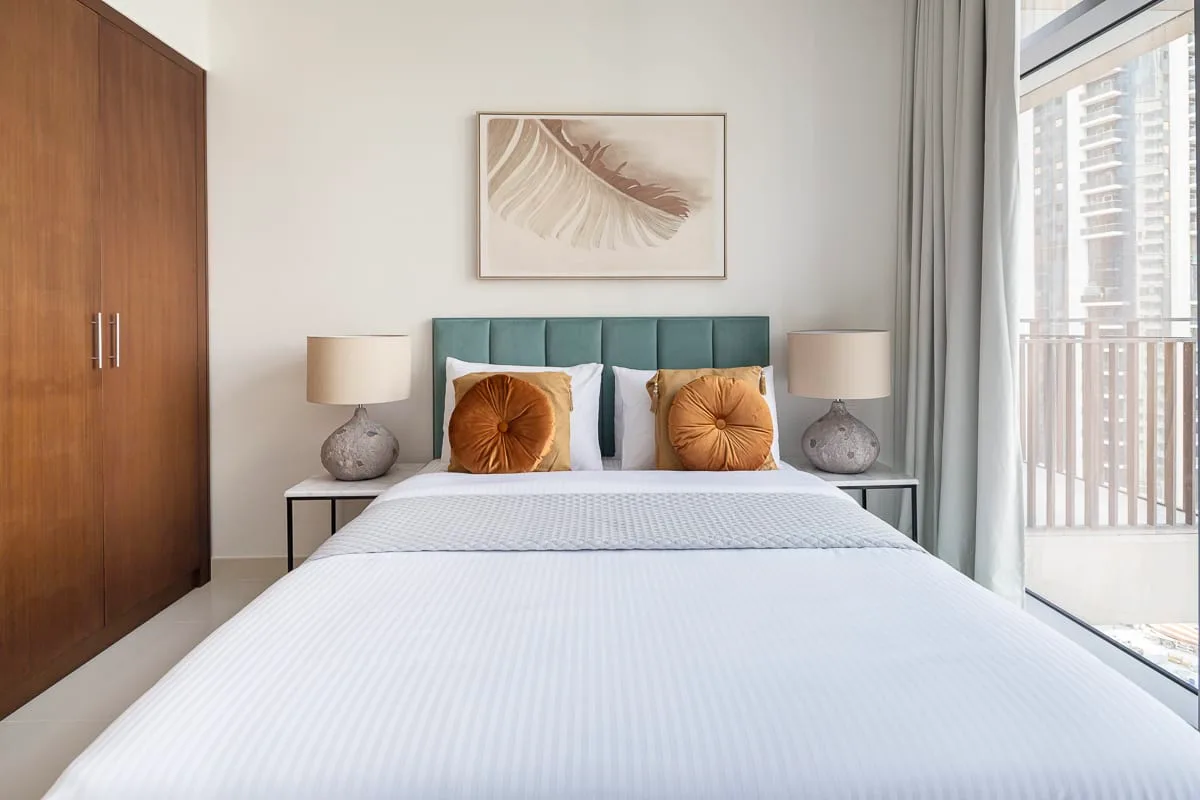 Un dormitorio con una cama, un cabecero verde azulado y una ventana amplia.