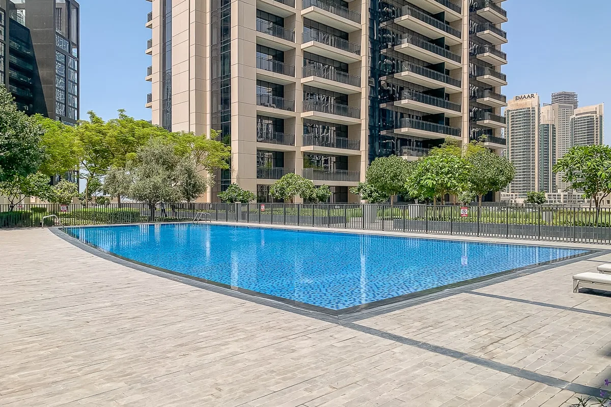 Una piscina al aire libre está junto a edificios residenciales altos y árboles.