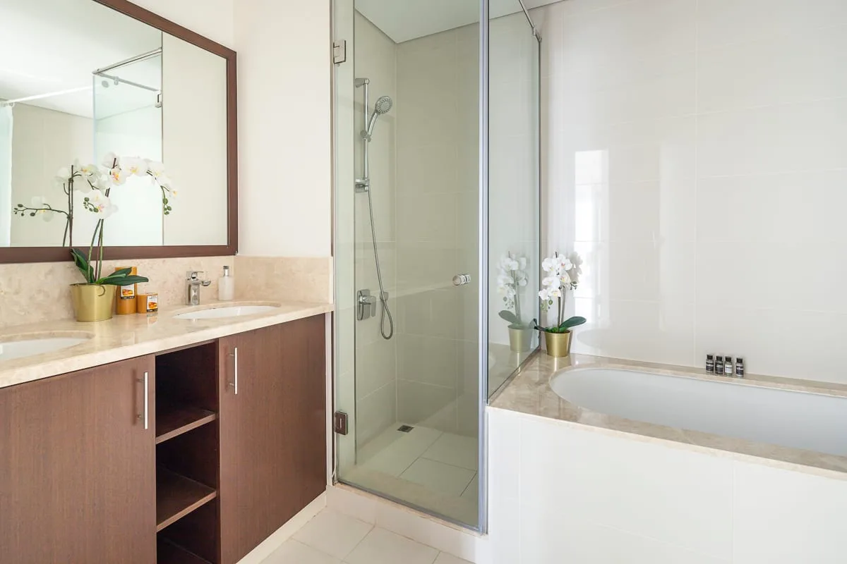 Un baño luminoso con ducha de vidrio, bañera y tocador.