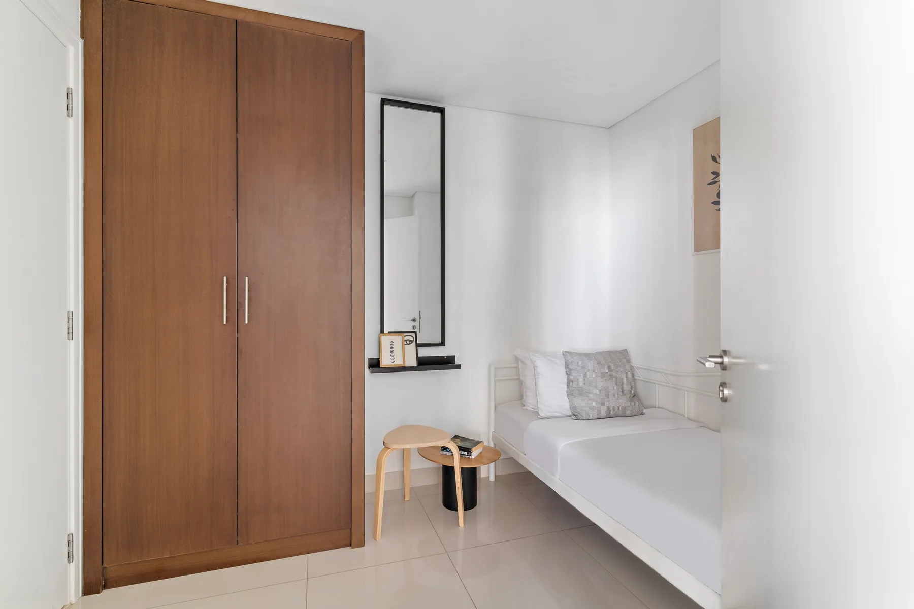 Un dormitorio luminoso con cama, armario de madera y una mesita.