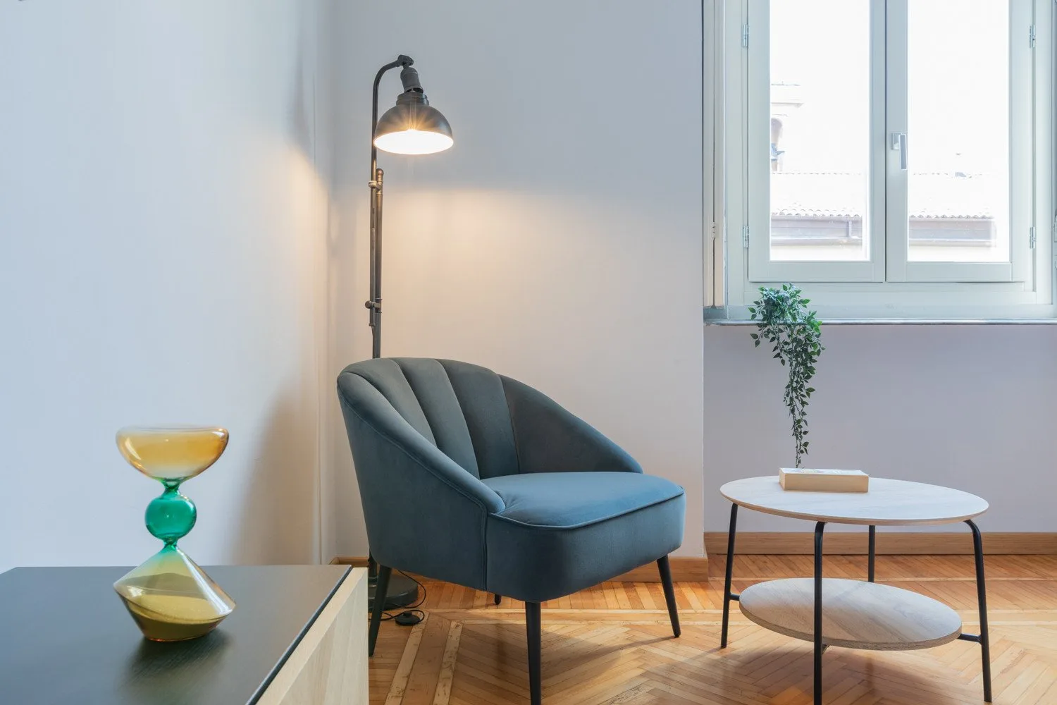 A seating area with a blue upholstered chair, floor lamp, and round table.