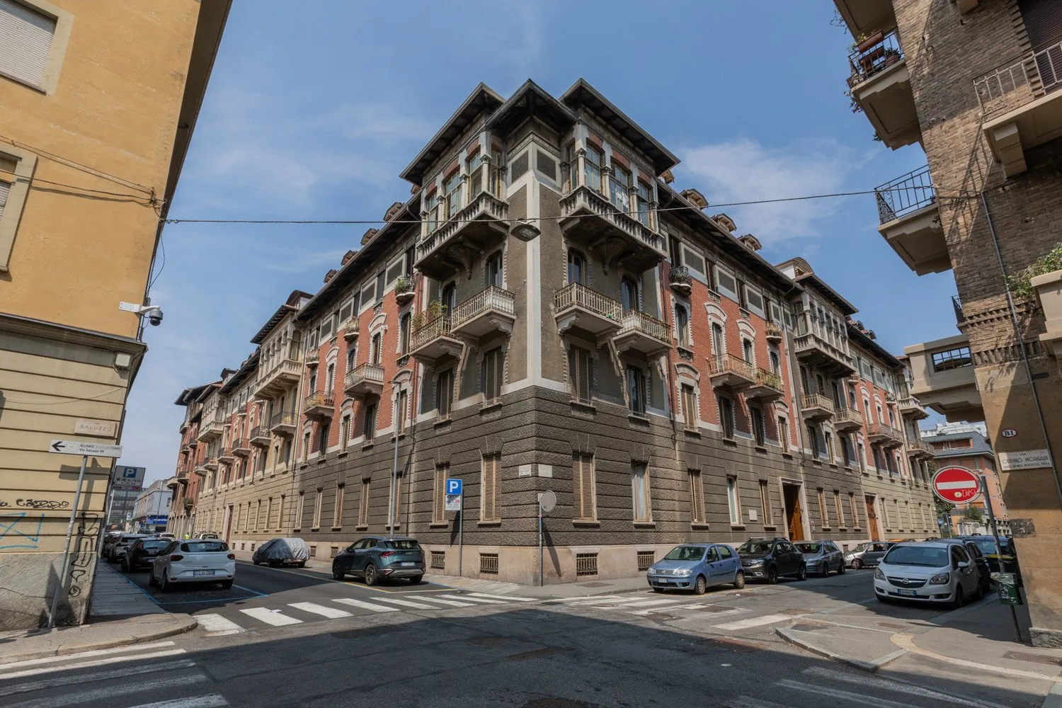 A large corner apartment building stands beside a city street and crosswalk.