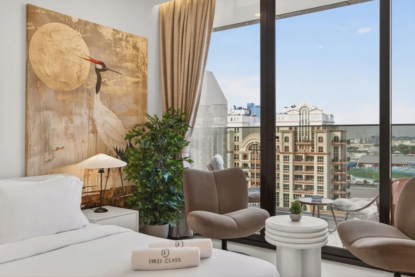 A bedroom seating area overlooks nearby buildings through large windows.
