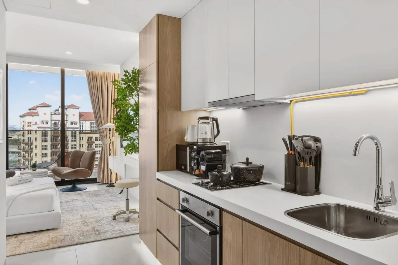A modern kitchen opens onto a living area with large windows.