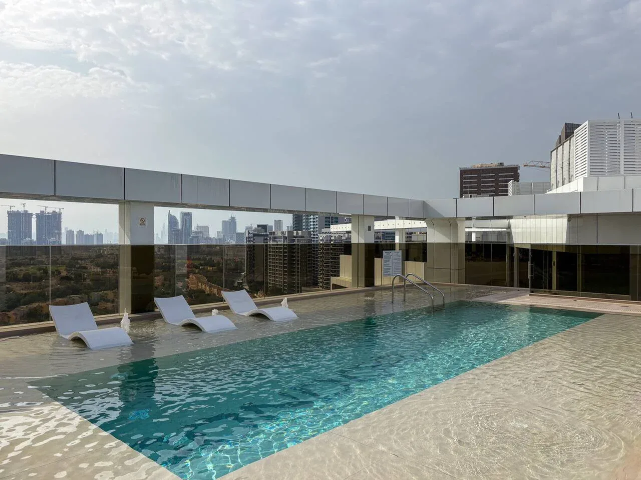 A rooftop swimming pool with lounge chairs and city views.
