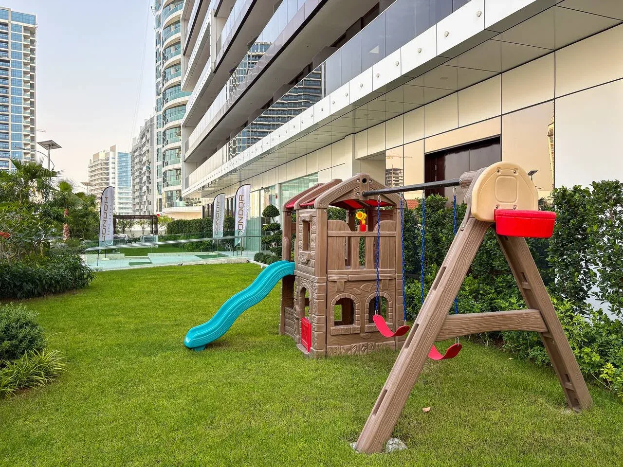 A grassy outdoor play area features a small play structure and a swing.