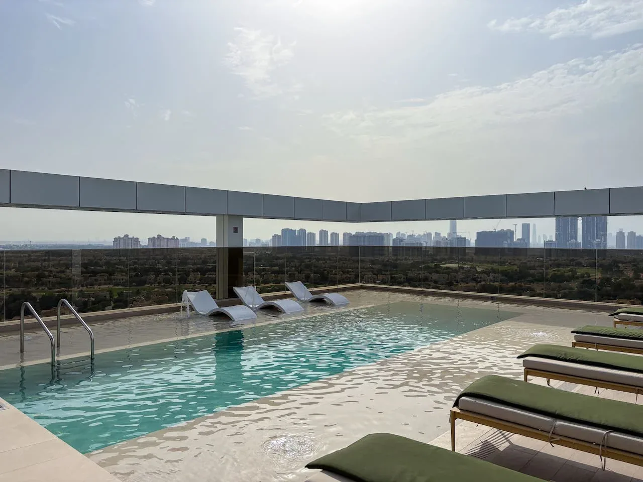 A rooftop swimming pool with lounge chairs overlooks a distant city skyline.