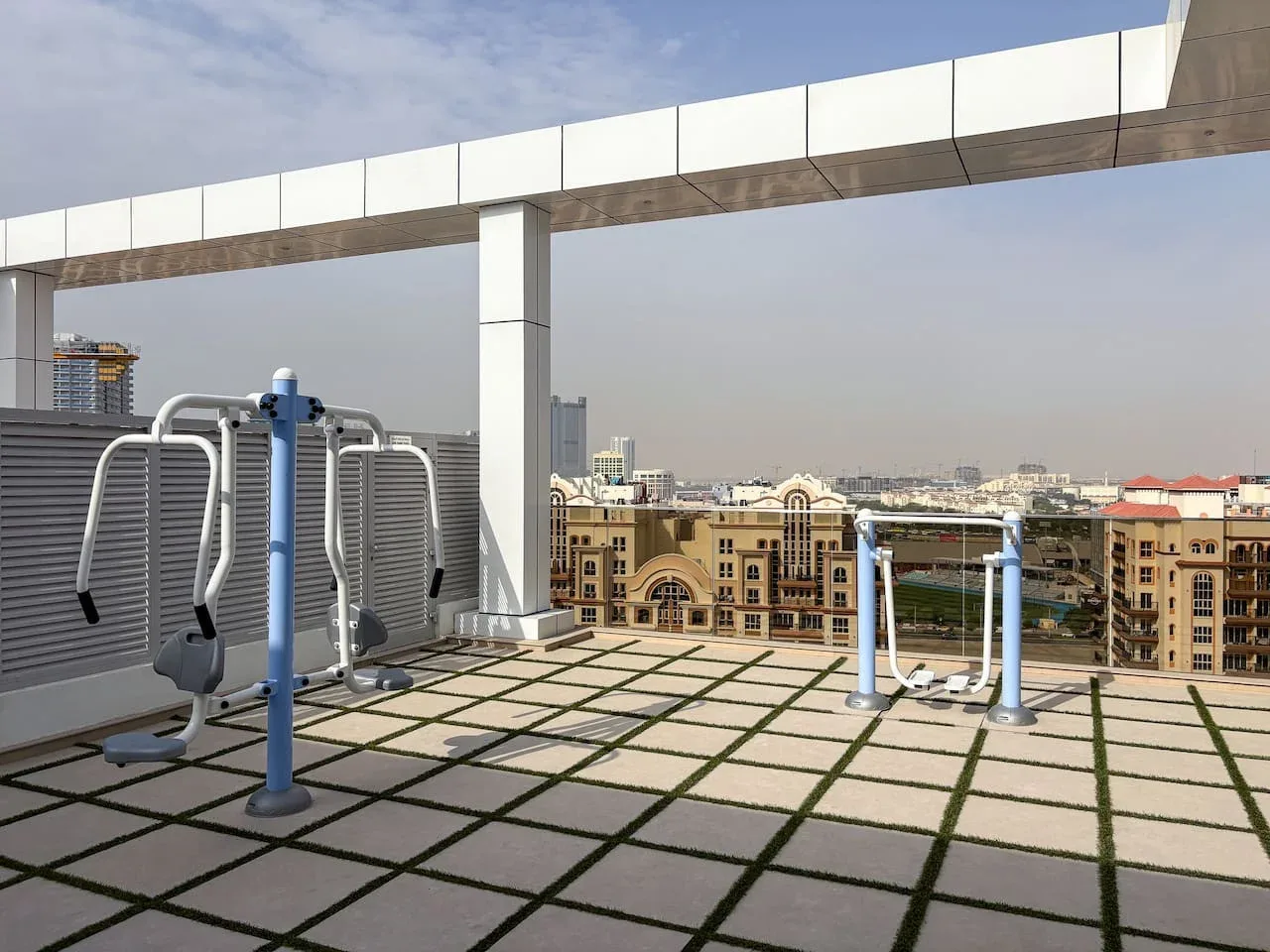 An outdoor exercise area with fitness equipment and city buildings in the background.
