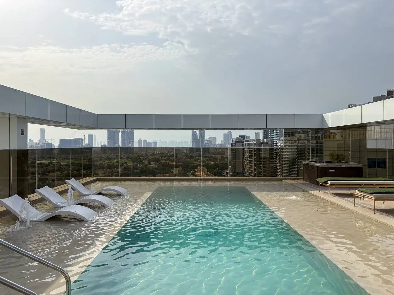 A rooftop swimming pool overlooks a city skyline, with loungers beside the water.