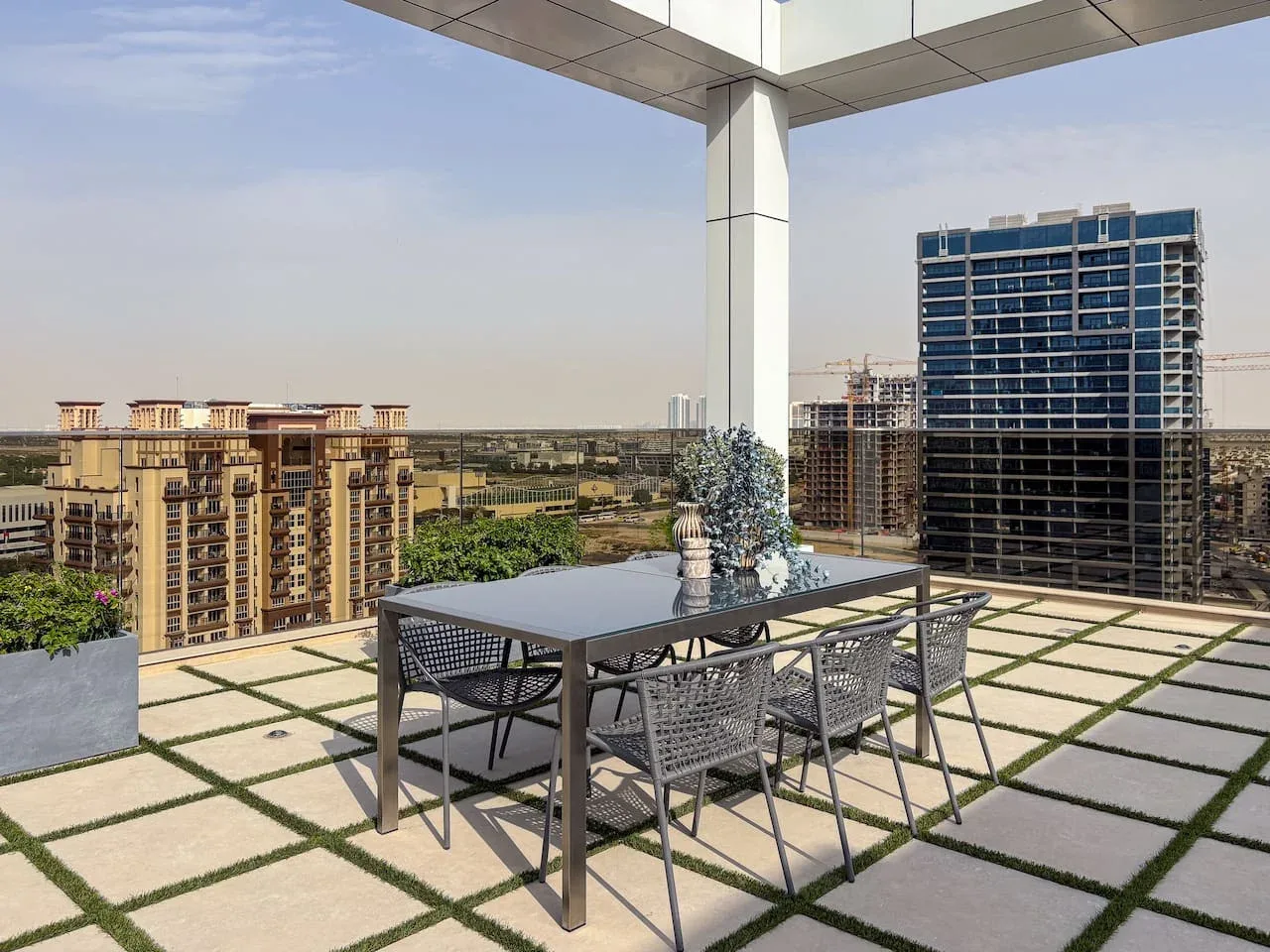 A rooftop terrace has an outdoor dining table and seating overlooking nearby buildings.