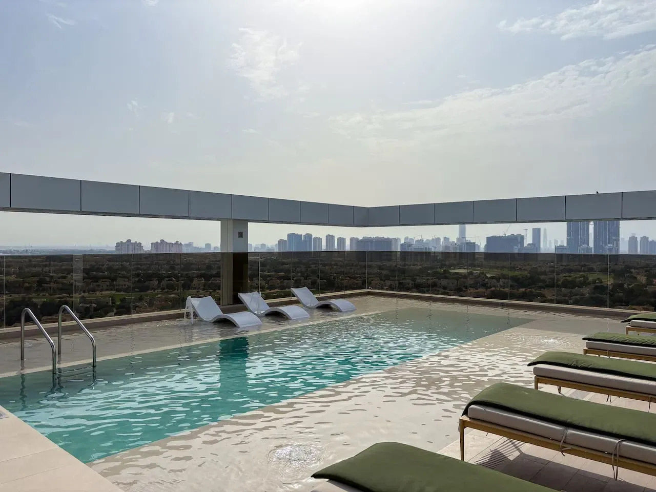 A rooftop pool with lounge chairs overlooks a distant city skyline.