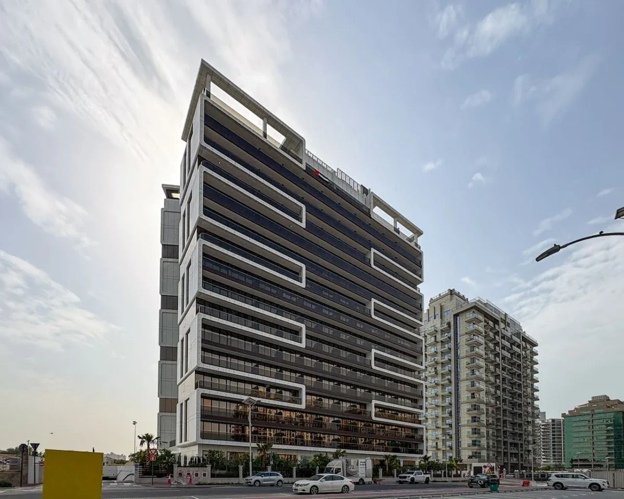 Modern multi-story buildings line a city street beneath a partly cloudy sky.