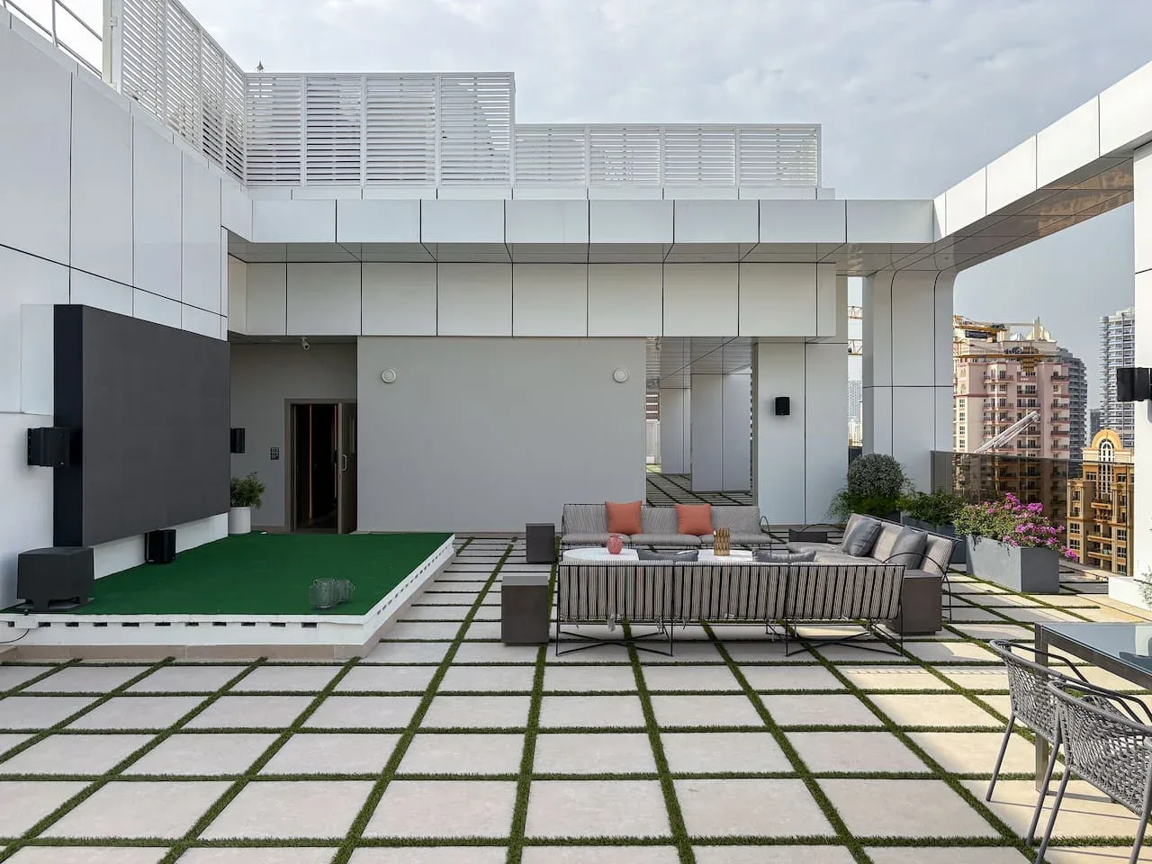 A rooftop terrace has a seating area beside a green artificial lawn.