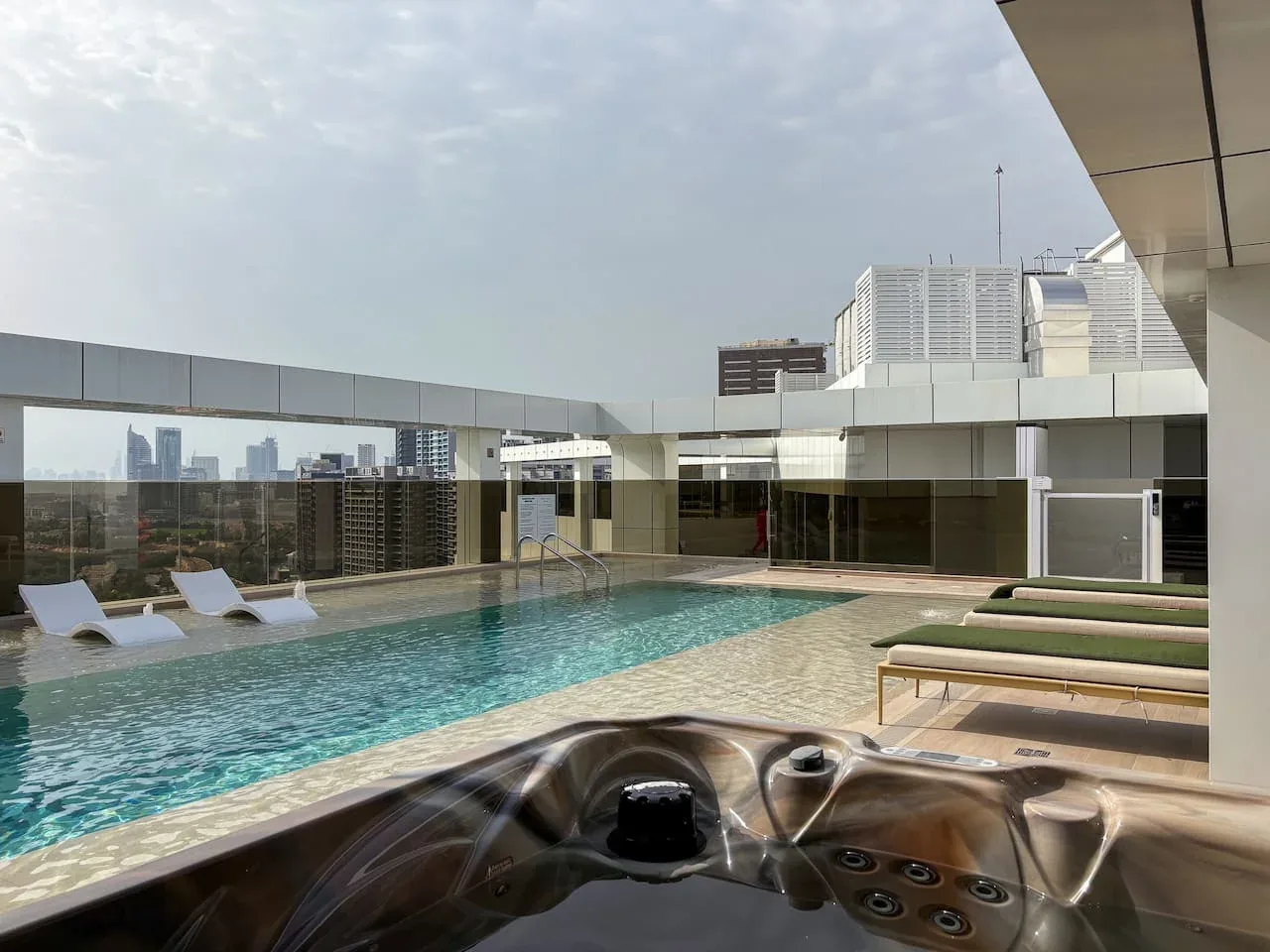 A rooftop pool and hot tub sit beside lounge chairs overlooking the city.
