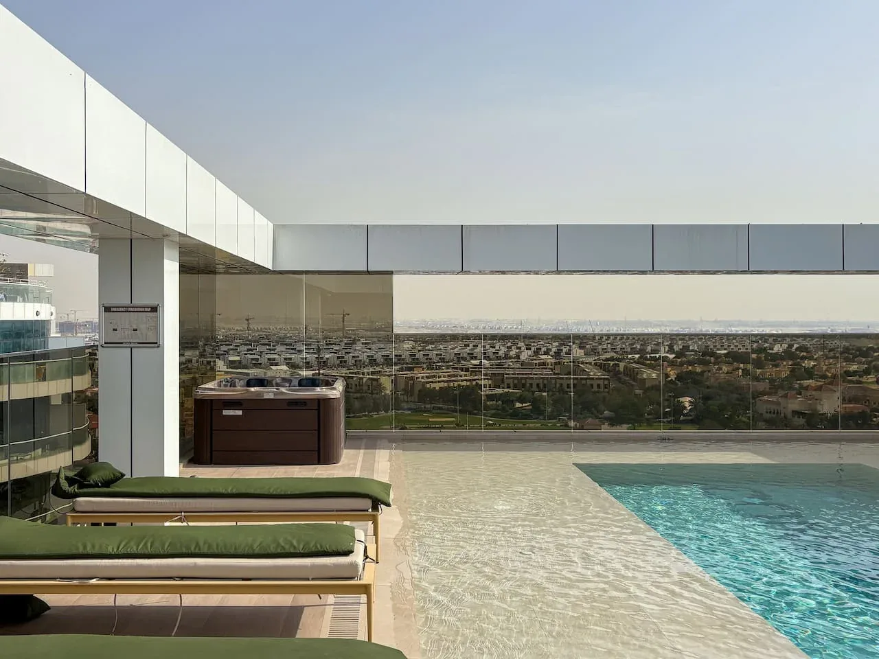 A rooftop pool area with a hot tub and a wide city view.