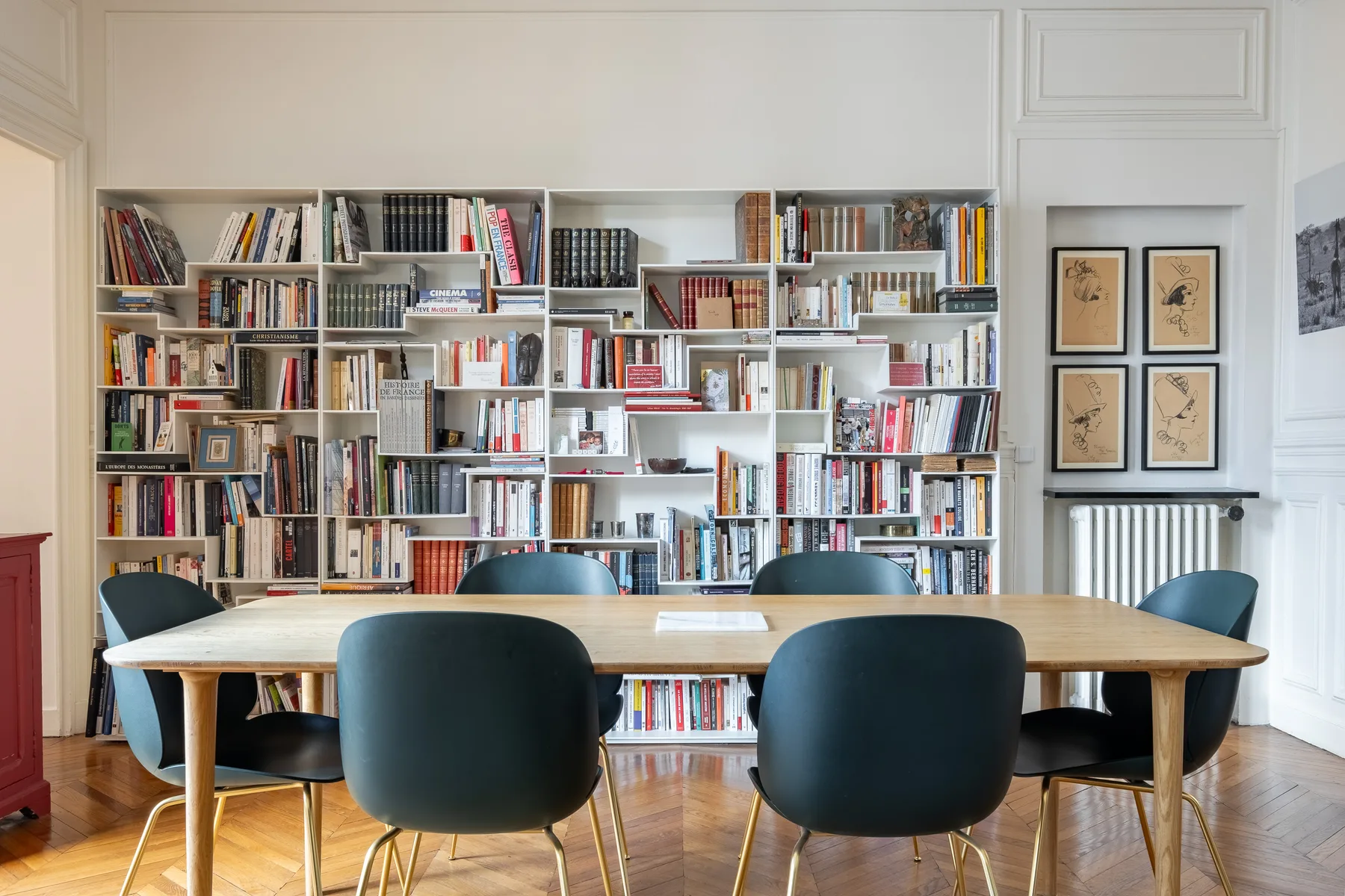 A dining table and chairs sit in front of a wall of bookshelves.
