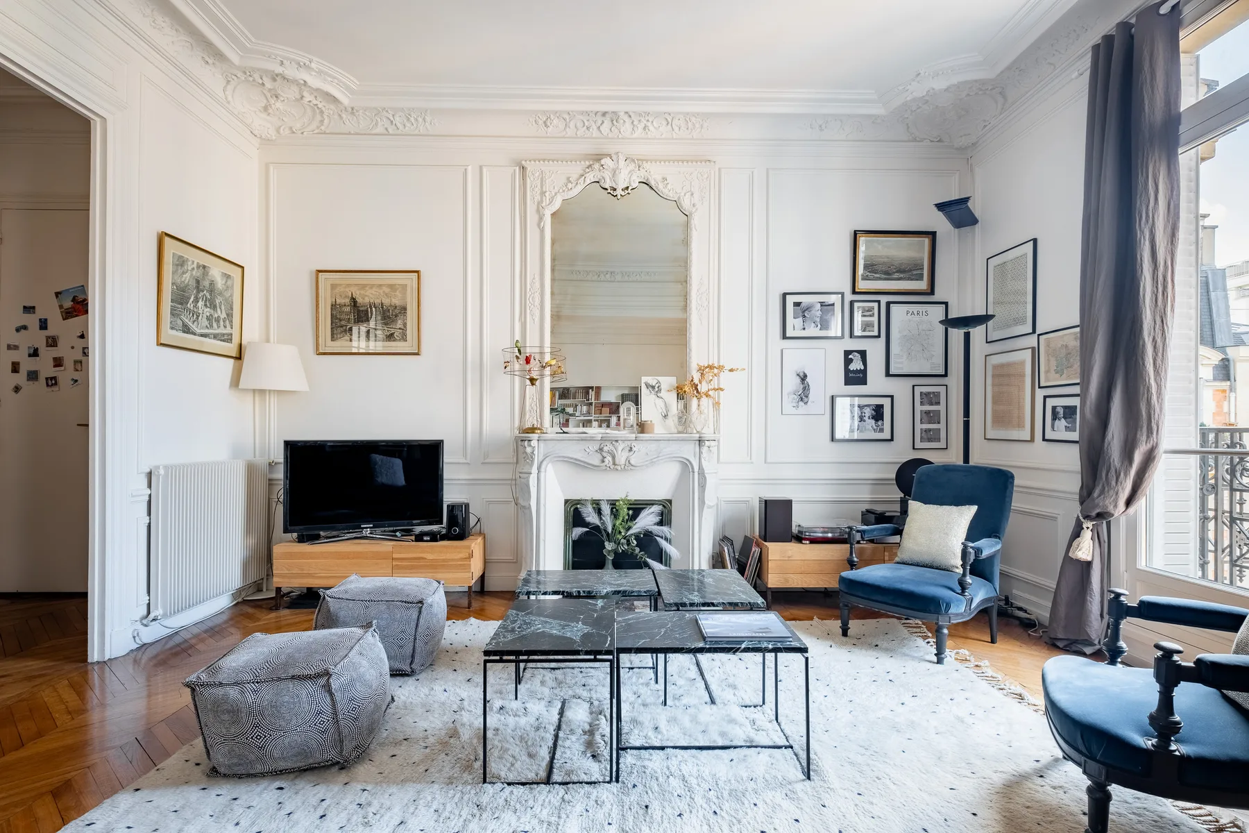 A bright living room with a fireplace, framed pictures, and seating around a coffee table.