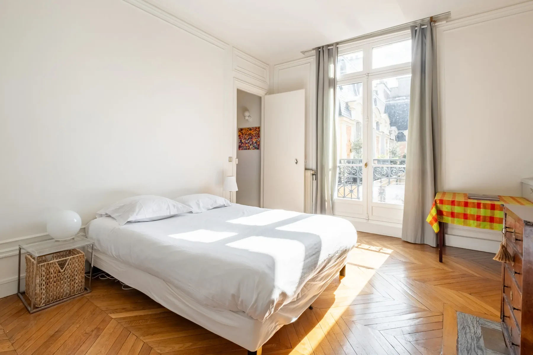 Un dormitorio luminoso con una cama junto a una ventana alta que da a un balcón.