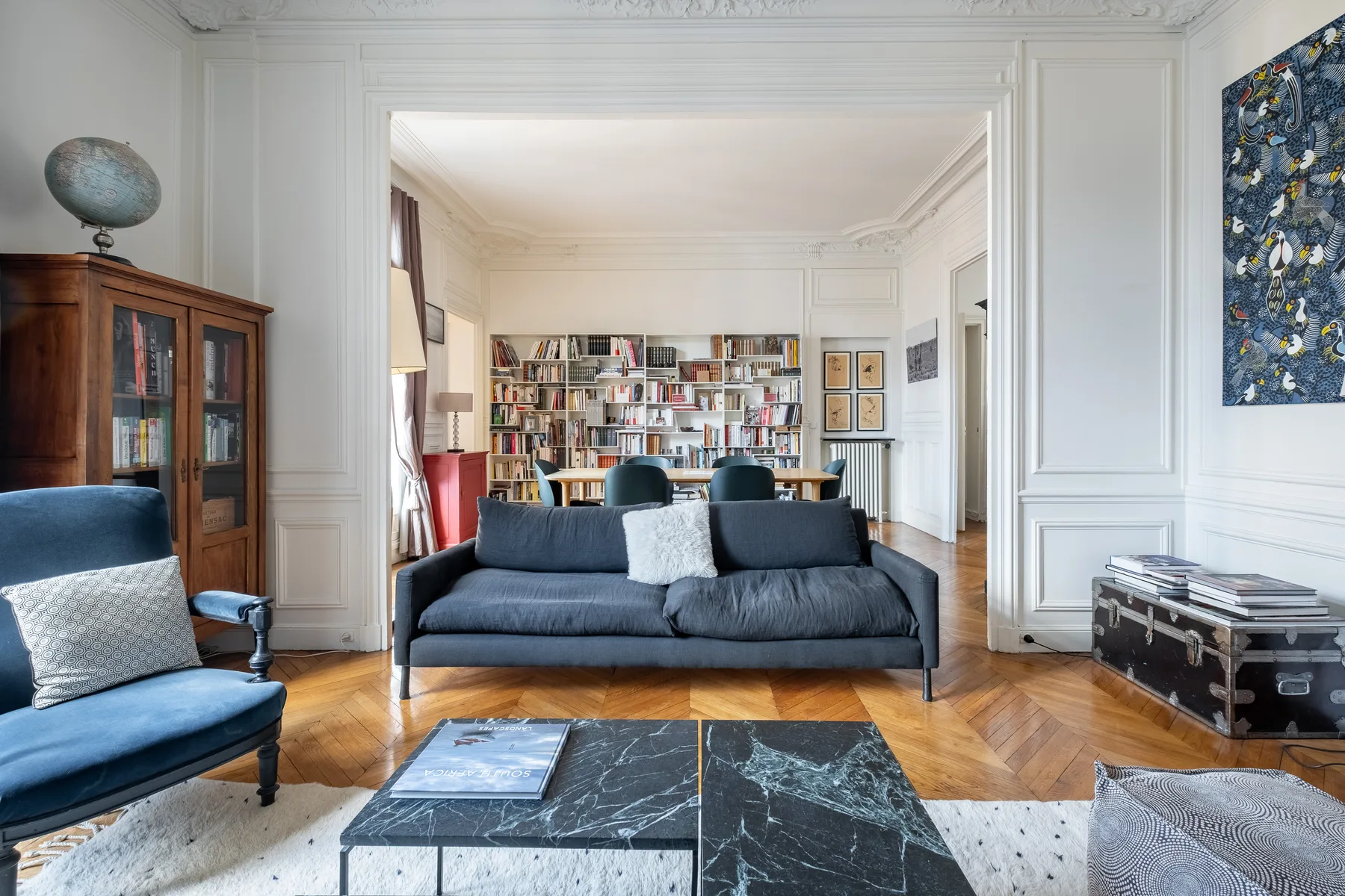 Una sala de estar con asientos azules, una mesa de centro y estanterías en la habitación contigua.