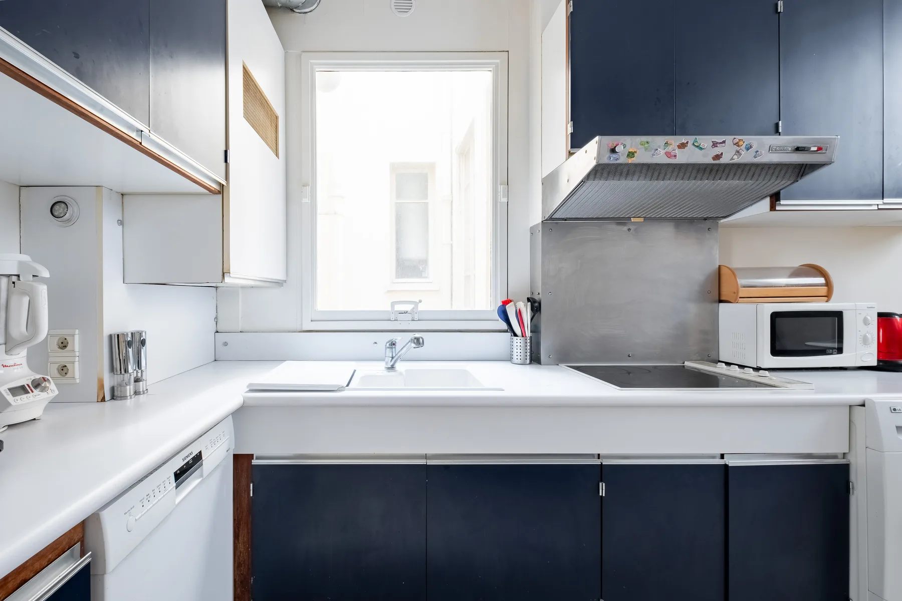Una cocina luminosa con gabinetes oscuros, encimeras blancas y una ventana sobre el fregadero.