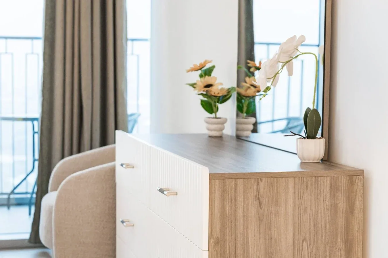 Zona de tocador en un dormitorio con cómoda de madera, espejo y pequeñas plantas en macetas.