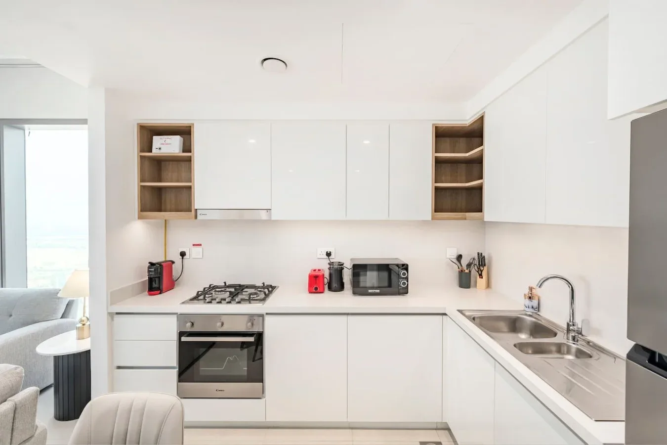 Una cocina blanca y luminosa con placa de cocina, horno y fregadero de acero inoxidable.