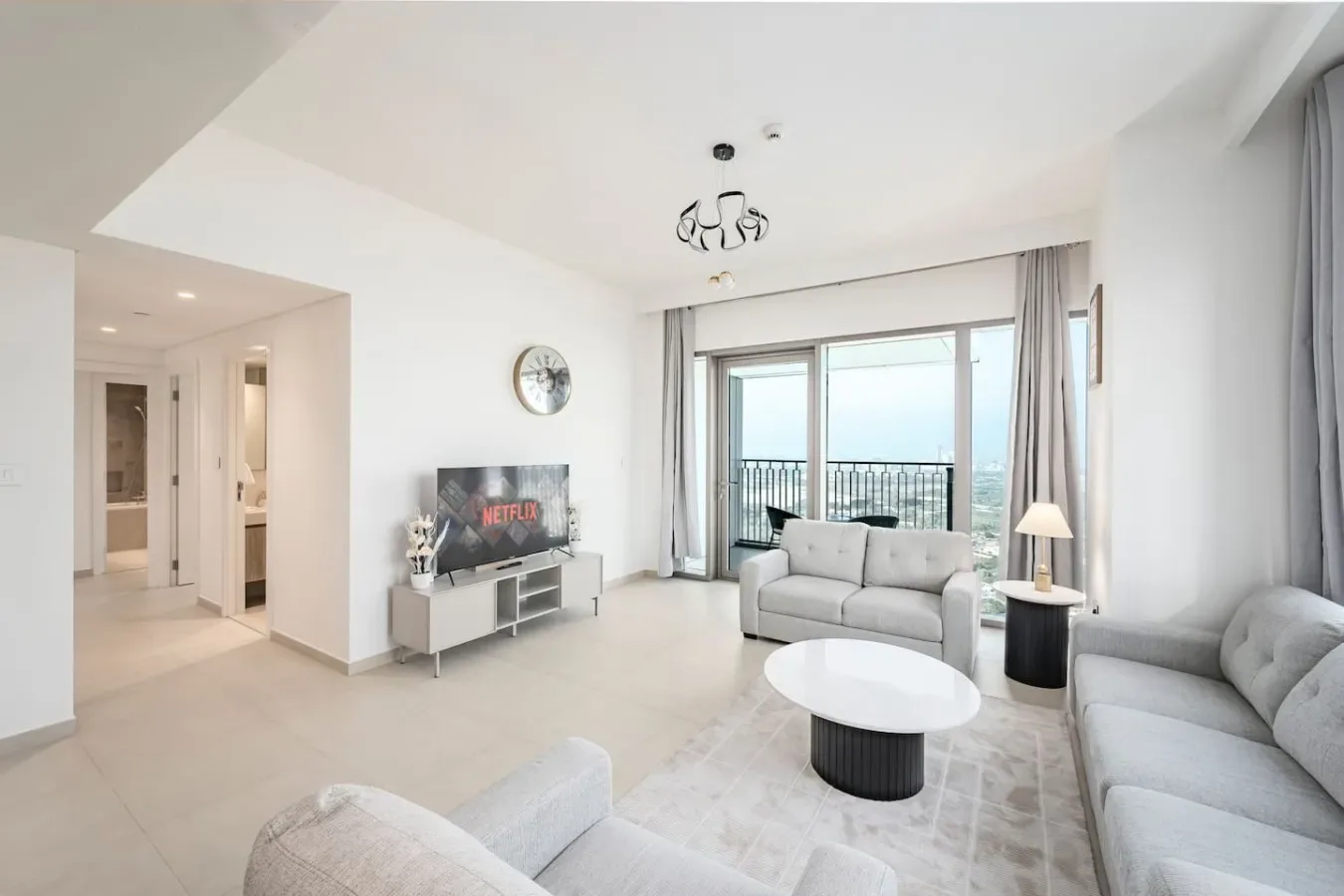 A bright living room with light seating, a round coffee table, and large windows.