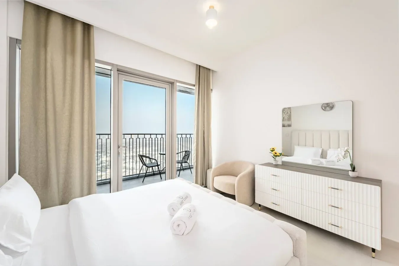 Un dormitorio luminoso con una cama, una cómoda y puertas de vidrio que dan a un balcón.