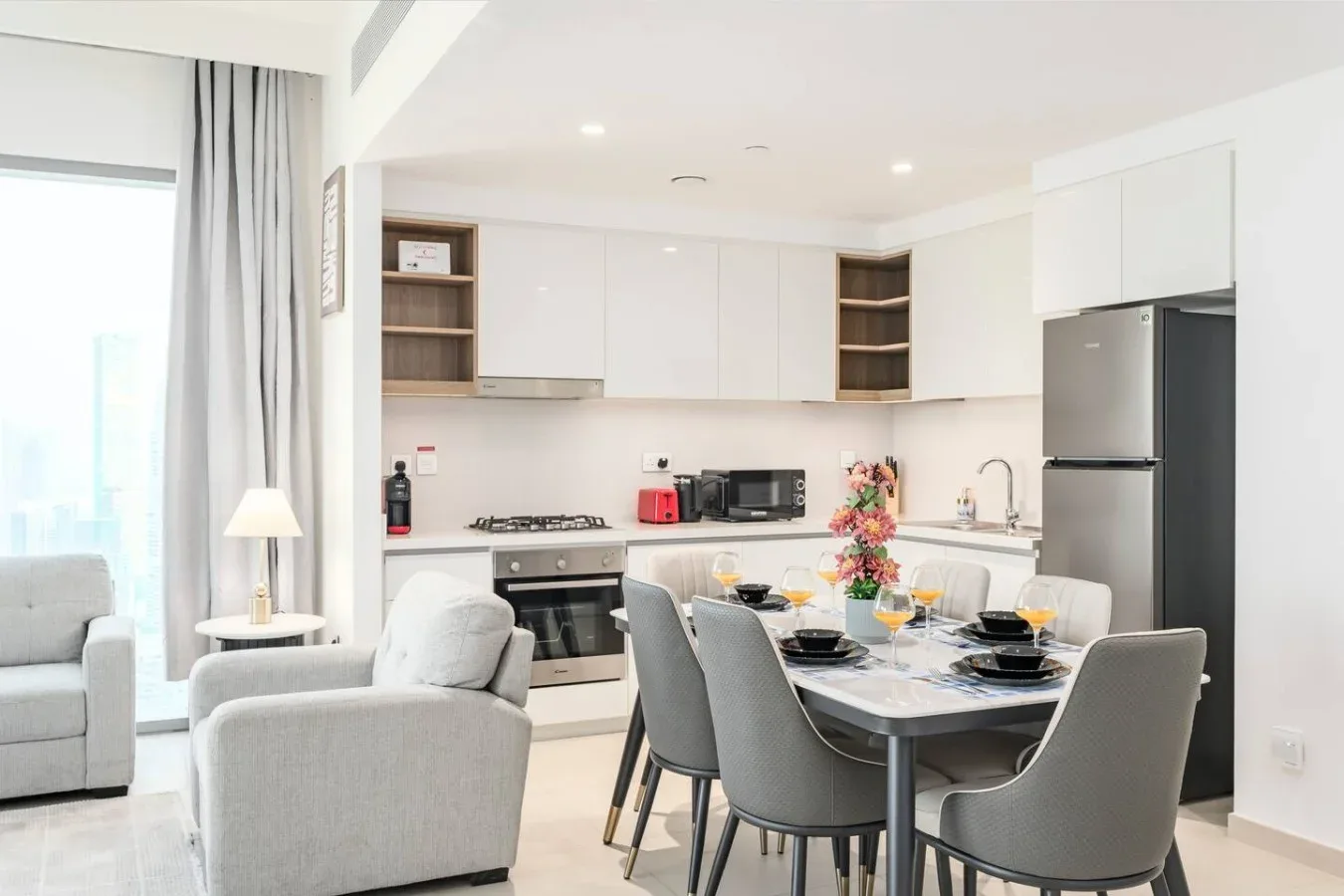 Una cocina y comedor luminosos con mesa, asientos y armarios blancos.
