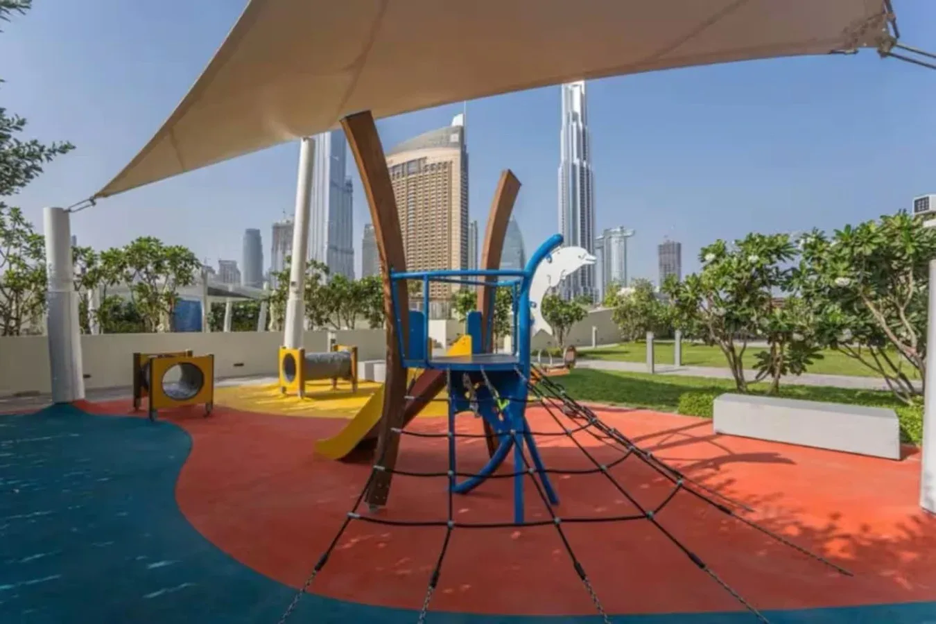 Un parque infantil al aire libre con juegos de colores está bajo una cubierta de sombra.