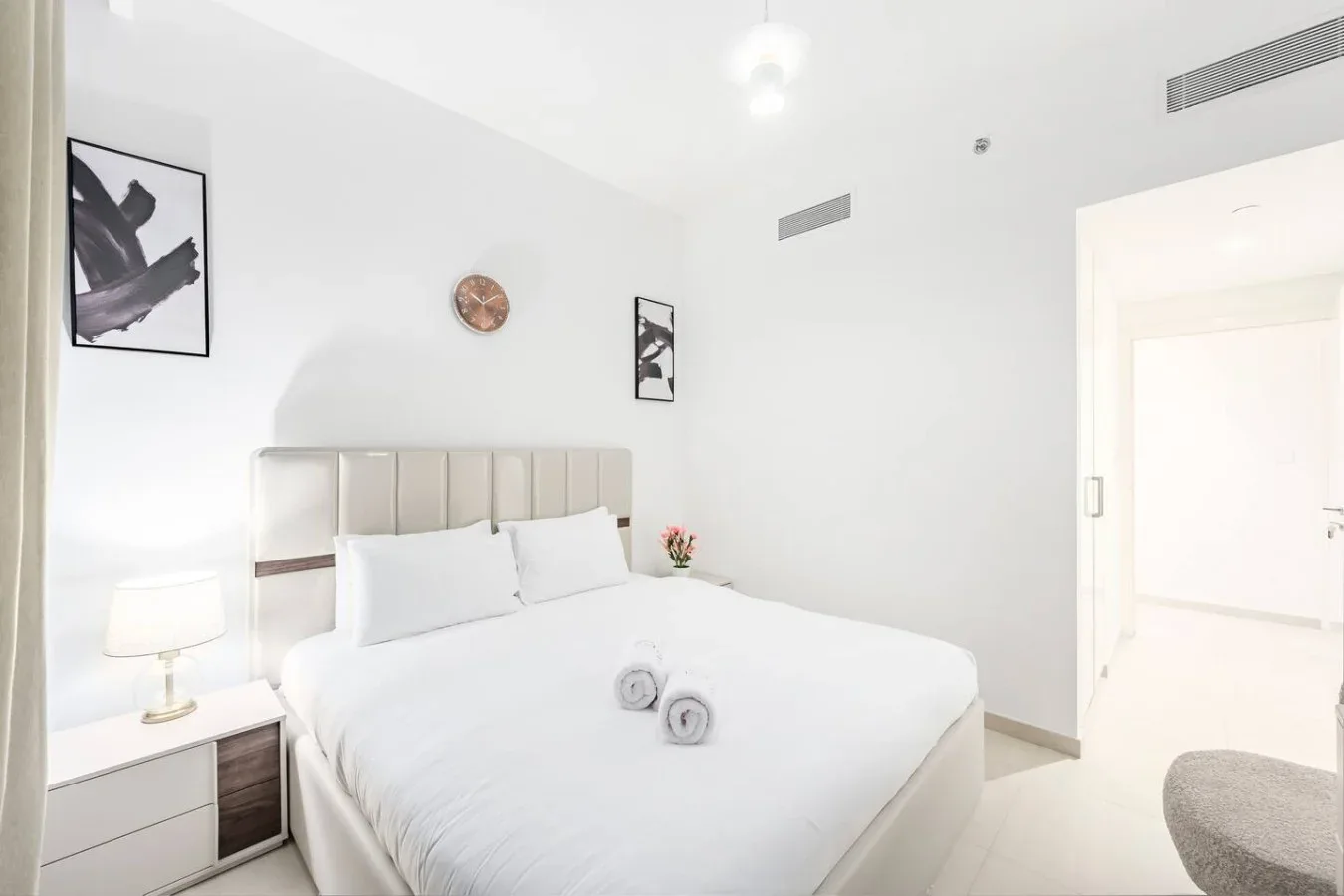 Un dormitorio luminoso con una cama bien tendida y cuadros en la pared.