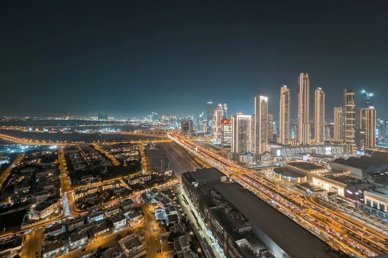 Un horizonte urbano nocturno con edificios altos iluminados y vías transitadas.