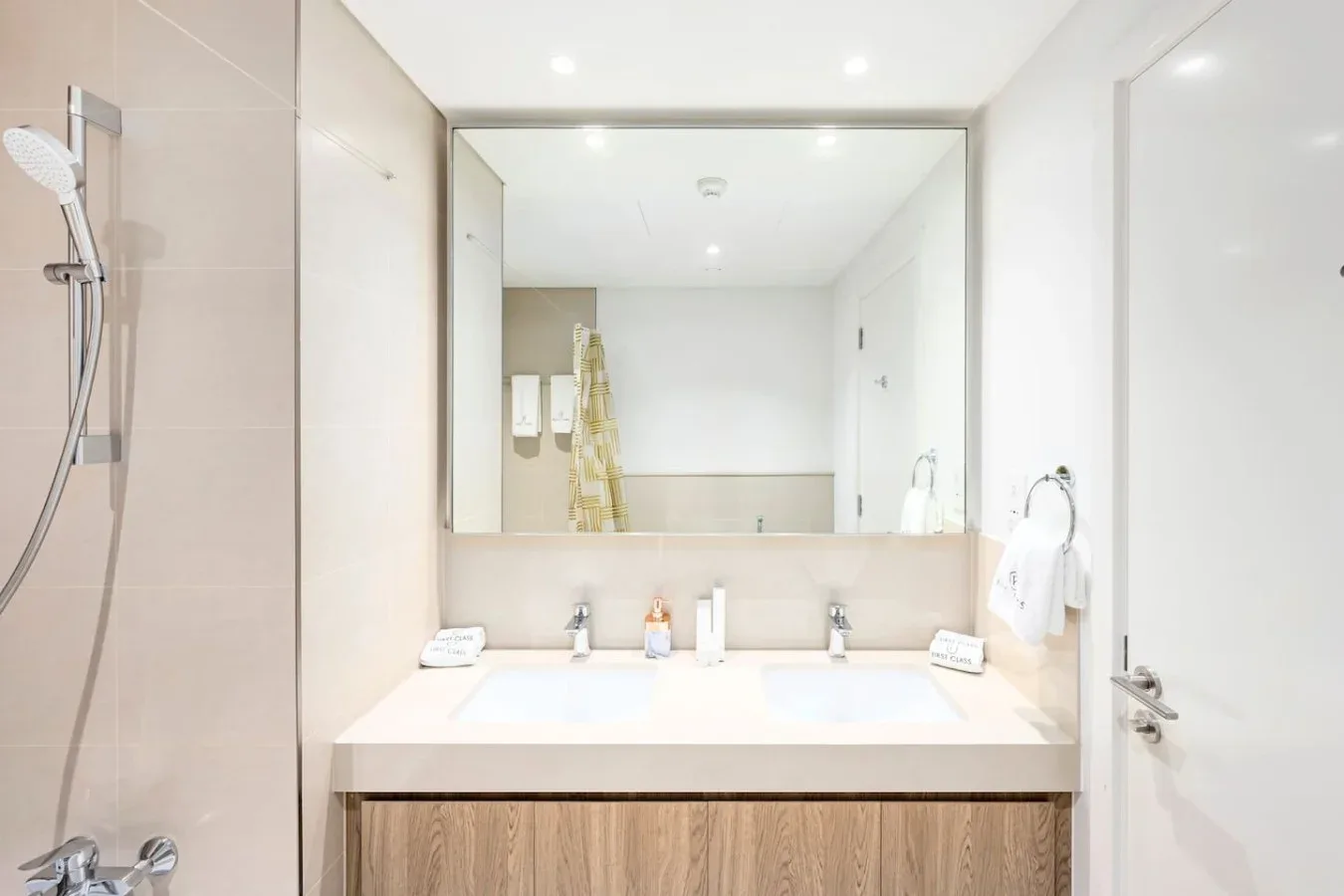 Un baño luminoso tiene un amplio tocador bajo un espejo grande y una ducha cerca.