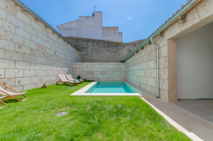 An outdoor pool sits beside a grassy courtyard enclosed by stone walls.
