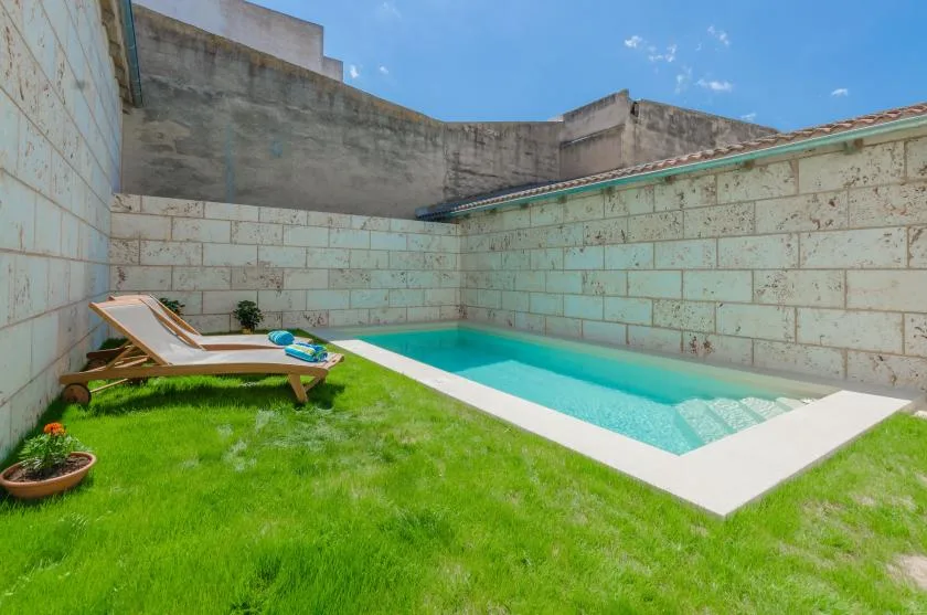 A small outdoor swimming pool sits beside a grassy lawn enclosed by stone walls.