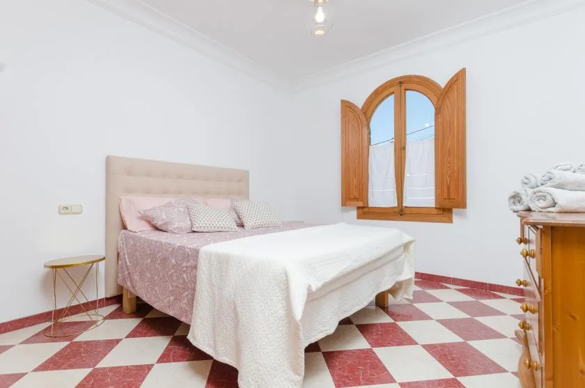 A bedroom with a bed, a red-and-white checkered floor, and a wooden window.