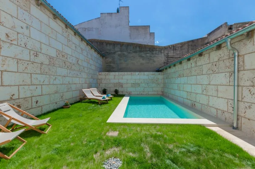 A small outdoor swimming pool sits beside a grassy lawn enclosed by high walls.