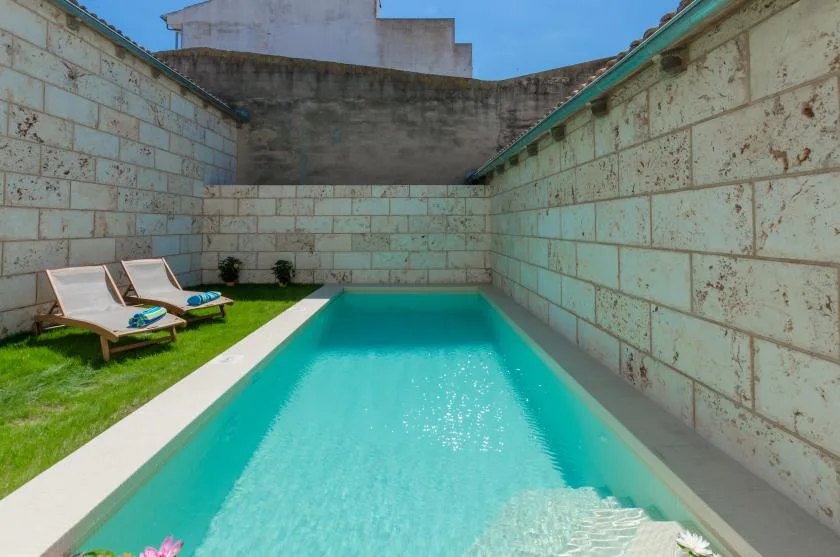 A narrow outdoor swimming pool sits between stone walls, with lounge chairs beside it.