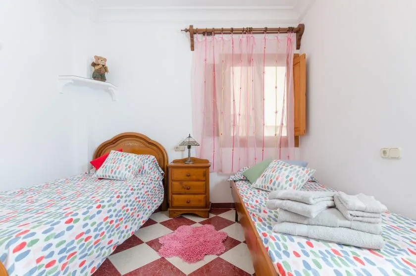A bedroom with two beds, patterned bedding, and a pink-curtained window.