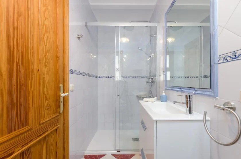 A tiled bathroom with a glass shower and a sink beside a wooden door.