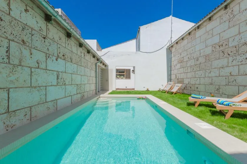 A narrow outdoor swimming pool runs between stone walls, with lounge chairs on the grass.